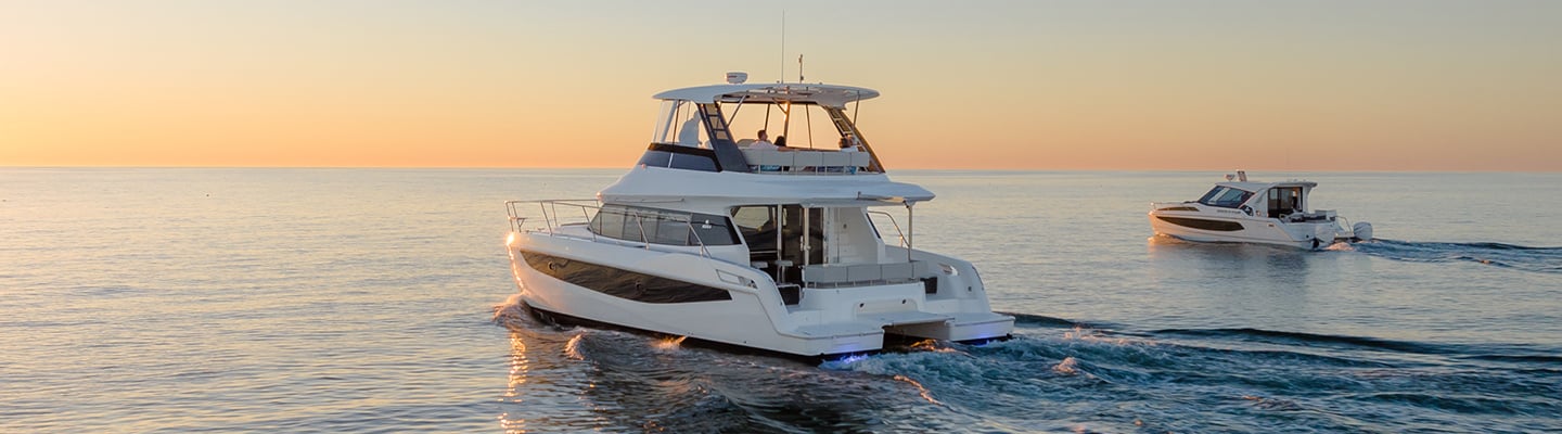 two Aquila Power Catamaran boats in the water with sunset in the background