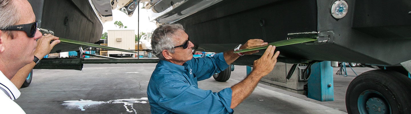 A man in a blue shirt holding a piece of metal up to the hull of a boat in a warehouse